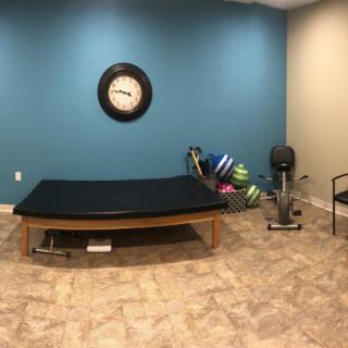 A therapy room with exercise equipment, a treatment table, and a clock on a blue wall.