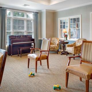 A cozy living room with a piano, several chairs, and large windows allowing natural light.