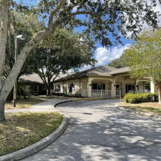 A view of a building with surrounding trees and a curved driveway under a partly cloudy sky.