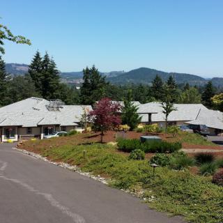 A scenic view of a building surrounded by trees and mountains under a clear blue sky.