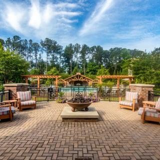 A beautiful outdoor patio with comfortable seating, a central fire pit, and a pergola overlooking a lush garden.