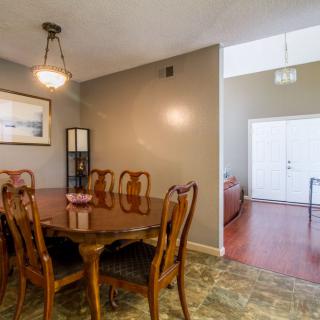A cozy dining room features a wooden table with chairs, adorned by a chandelier and complemented by floor tiles.