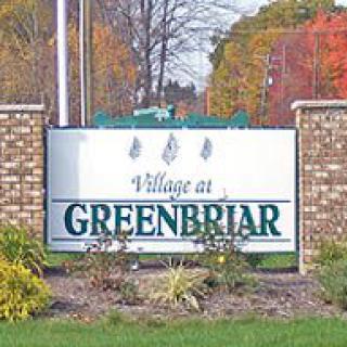 Entrance sign for the Village at Greenbriar with brick pillars and autumn foliage.