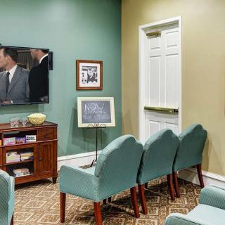 A cozy waiting room with teal chairs, a television, and wall art.