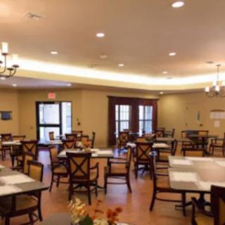 An empty dining room with neatly arranged tables and chairs, illuminated by overhead lighting.