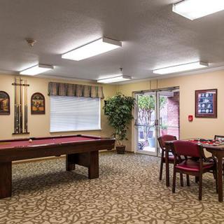 A cozy recreation room featuring a pool table, card table with chairs, and decorative wall art.