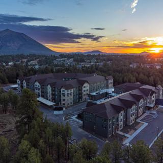 A scenic aerial view of buildings surrounded by trees with a mountain backdrop at sunset.