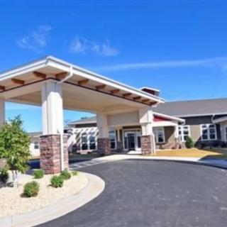 A modern building with a covered entrance and landscaped surroundings under a clear blue sky.