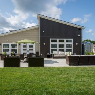 A modern house with a spacious patio and outdoor seating, surrounded by a well-maintained lawn on a sunny day.
