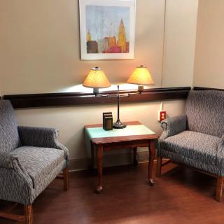 A cozy waiting area with two armchairs, a small table with a lamp, and a painting on the wall.