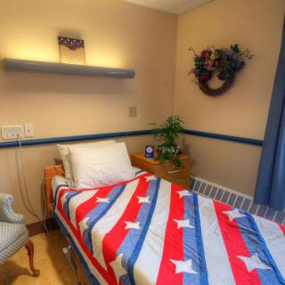 A small bedroom or hospital room with a single bed covered in a patriotic-themed blanket.