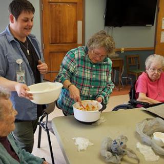 A lively cooking activity taking place at a community center, where seniors are engaged in preparing a dish together.