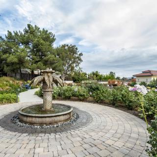 A scenic garden with a central stone fountain and surrounding greenery.