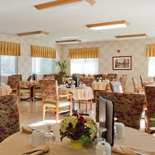 A cozy dining area with neatly arranged tables and chairs, featuring large windows with striped curtains.