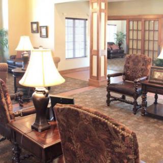 A warmly decorated living room with upholstered chairs, lamps, and a wooden table.