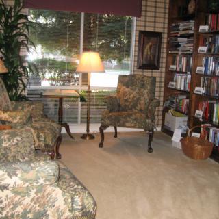 A cozy living room with a bookshelf, armchairs, and a large window bringing in natural light.
