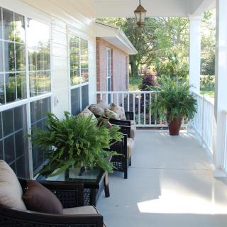 A cozy porch area with outdoor seating and lush plants, bathed in sunlight.