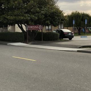 A parking lot with cars and a visible sign near a road and trees.