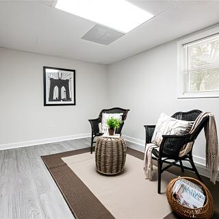 A minimalist room with two chairs, an indoor plant on a small table, and framed artwork on the wall.