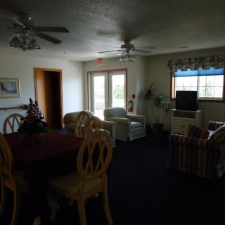 A cozy living room with a TV, chairs, and a dining table near the windows.