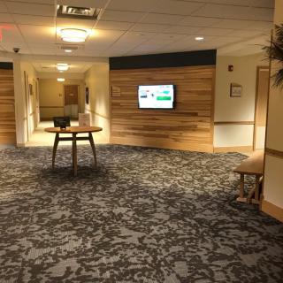 A modern hallway with carpet flooring, wood paneling, and a mounted television.