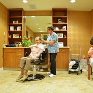 A hairdresser provides a haircut to a senior in a salon setting, emphasizing care and service.