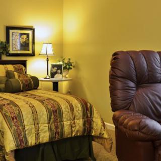 A cozy bedroom featuring a patterned bedspread and a leather armchair, illuminated by soft lighting from a bedside lamp.