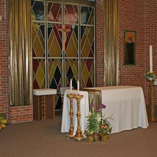 A church interior featuring an altar with flower arrangements and a backdrop of stained glass windows.