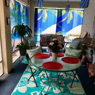A cozy patio area featuring a round dining table with red placemats, surrounded by cushioned chairs and vibrant tropical decor.