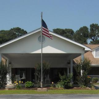 A residential building with an American flag flying, surrounded by a garden and trees.