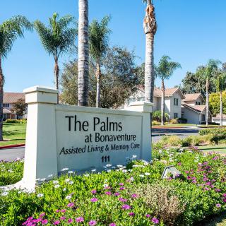 The entrance sign of The Palms at Bonaventure, an assisted living and memory care community, surrounded by palm trees and colorful flowers.