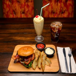 A delicious burger served with crispy fries, a classic milkshake, and a glass of soda.