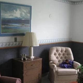 A cozy living room corner featuring a cushioned chair, a wooden side table with a lamp, and a painting on the wall.