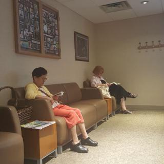 Two people sitting in a waiting room, occupying themselves with reading and using a smartphone.