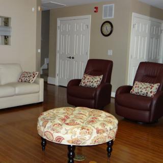 A cozy living room featuring a white sofa, two brown recliners with patterned pillows, and a floral ottoman on a hardwood floor.