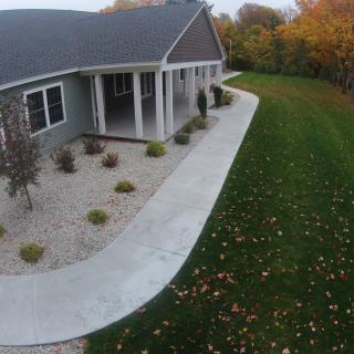 A house with a surrounding sidewalk, neatly landscaped lawn and trees displaying autumn colors.