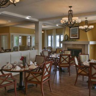 An elegantly designed restaurant dining area with neatly arranged tables and chairs, adorned with chandeliers and a cozy fireplace.