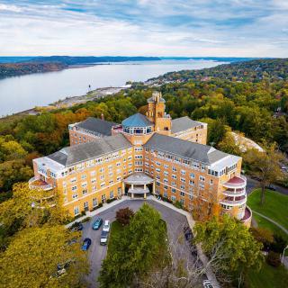 Aerial view of a large building surrounded by trees with a river in the background.
