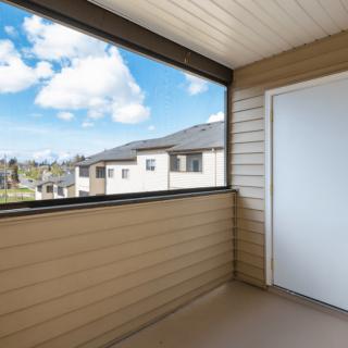 A residential balcony overlooking a neighboring building, featuring a clear blue sky and clouds.
