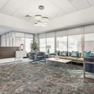 A modern office waiting area with a reception desk, comfortable seating, and large windows providing natural light.