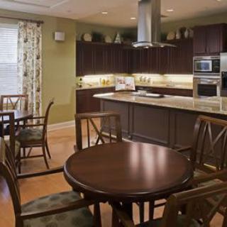 A modern kitchen with an adjacent dining area, featuring dark cabinets and a central table with chairs.