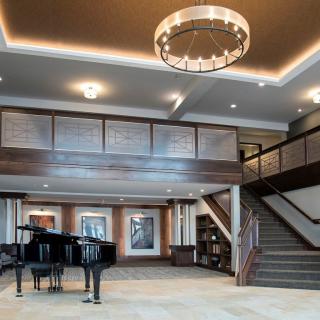 A spacious modern lobby with a grand piano, chandelier, and staircase.