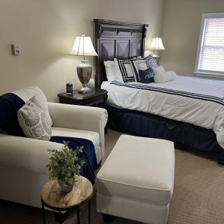 A cozy bedroom with a neatly made bed, a comfortable armchair, and elegant lighting.