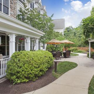 A scenic outdoor area featuring a building, lush greenery, and a winding pathway leading to a patio with umbrellas.