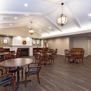 A spacious dining area featuring multiple tables and chairs, with elegant lighting and a wooden floor.