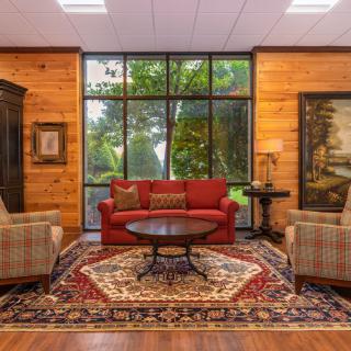 A cozy living room with wood paneling, featuring a red sofa, armchairs, and a decorative rug.