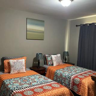 A cozy bedroom with two twin beds, each adorned with colorful bedding and orange accents. A painting hangs above the beds, and lamps are placed on either side for ambient lighting.