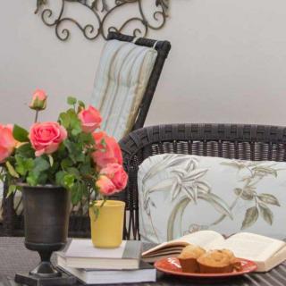 A cozy outdoor seating area with a vase of roses, books, and a plate of cookies on a coffee table.