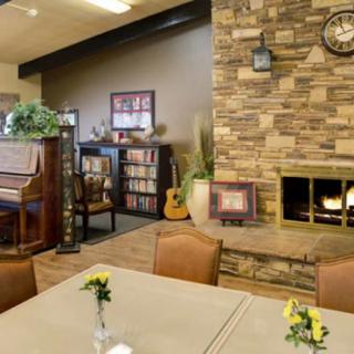A cozy living room features a stone fireplace, piano, and bookshelf.