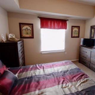 Cozy bedroom with a striped bedspread, dresser, and a small TV under a window with red valance.